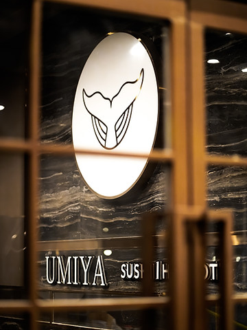 Lit whale-tail logo sign behind the wooden lattice at the Umiya Raleigh entrance